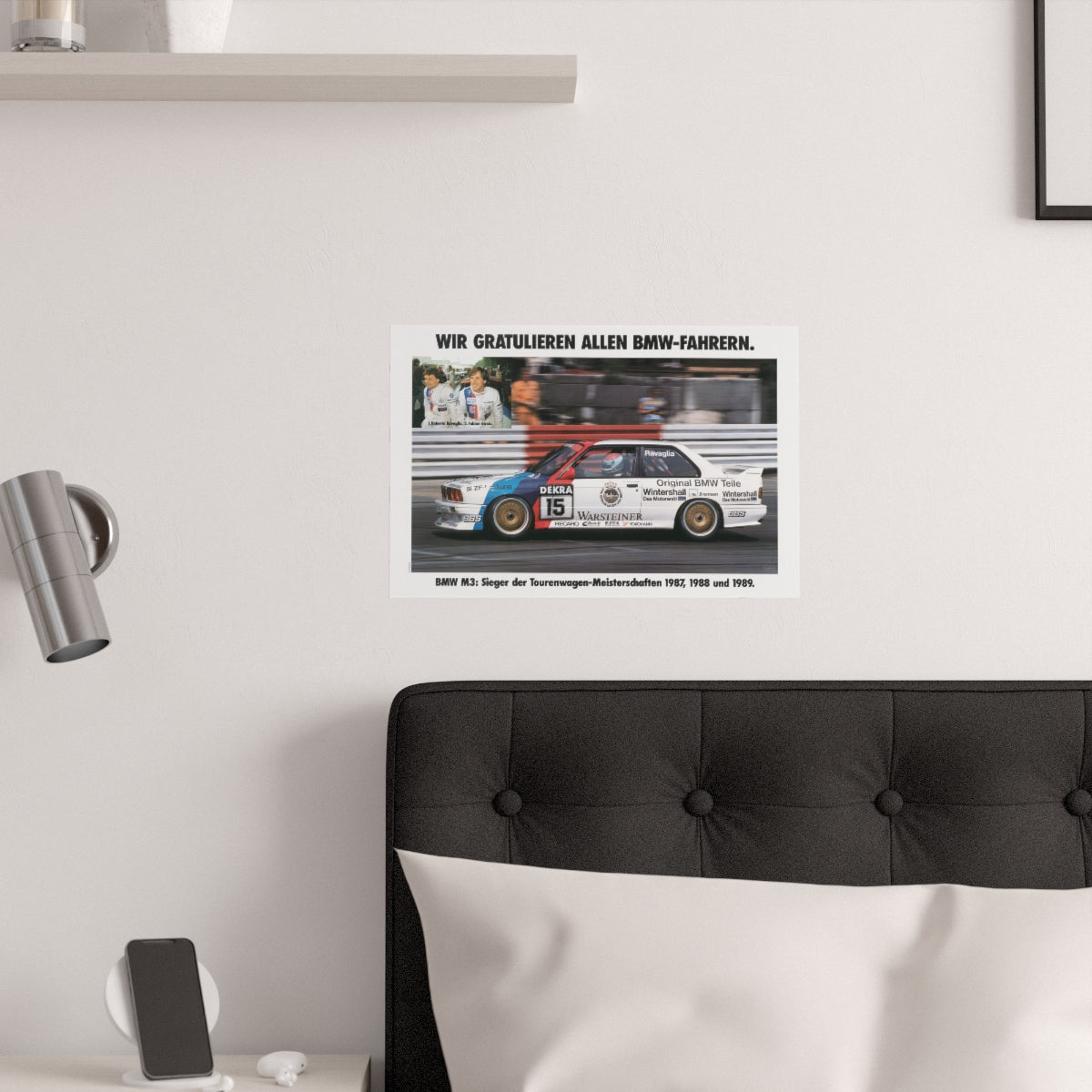 BMW E30 M3 shown in motion, racing on a track. Title above the photo reads Congratulations to all BMW drivers. The poster is displayed in a white bedroom and placed over dark gray headboard.