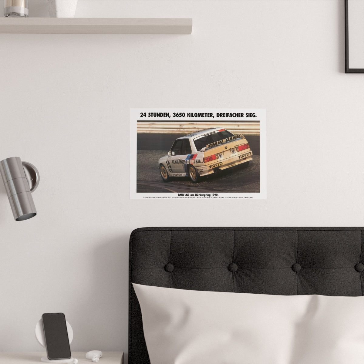 BMW E30 M3 shown racing on the iconic Carousel corner at the Nurburgring track in Germany. Title of the picture reads "24 Hours, 3650 kilometers, triple victory". The poster is displayed in a white bedroom and placed over dark gray headboard.