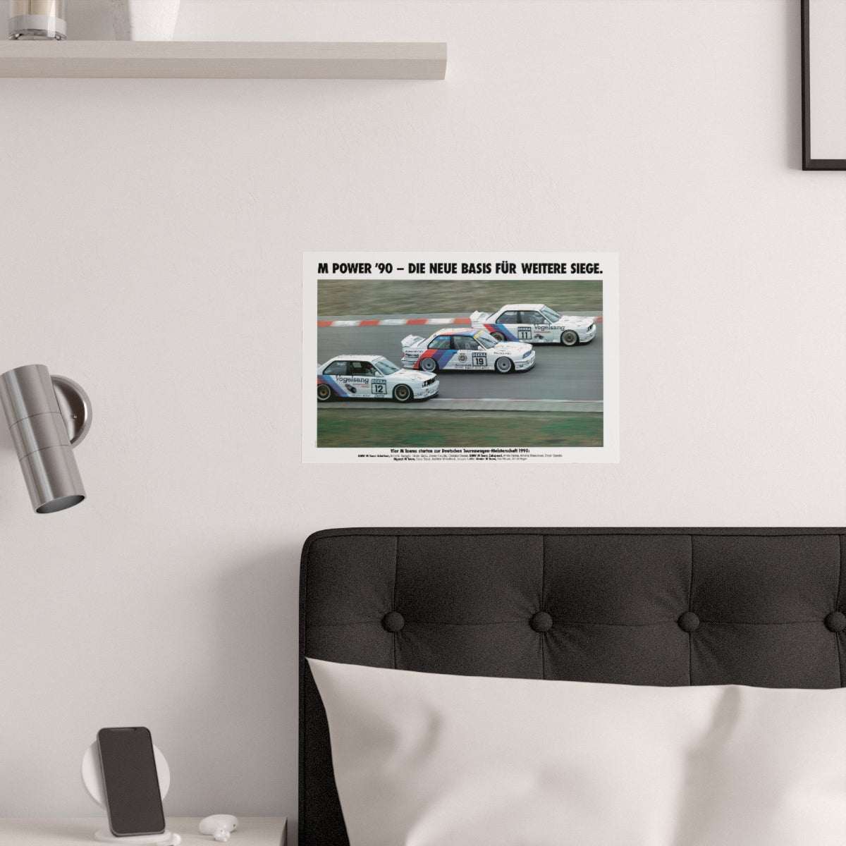 Three BMW E30 M3 race cars shown in motion, racing on a track. Title above the photo reads M Power '90 - The new basis for further victories. The poster is displayed in a white bedroom and placed over dark gray headboard.