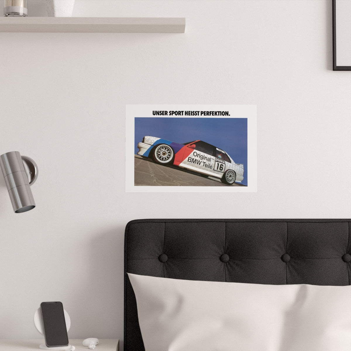 BMW E30 M3 race car shown from the side with a title above it that reads: Our sport is called perfection. The poster is displayed in a white bedroom and placed over dark gray headboard.