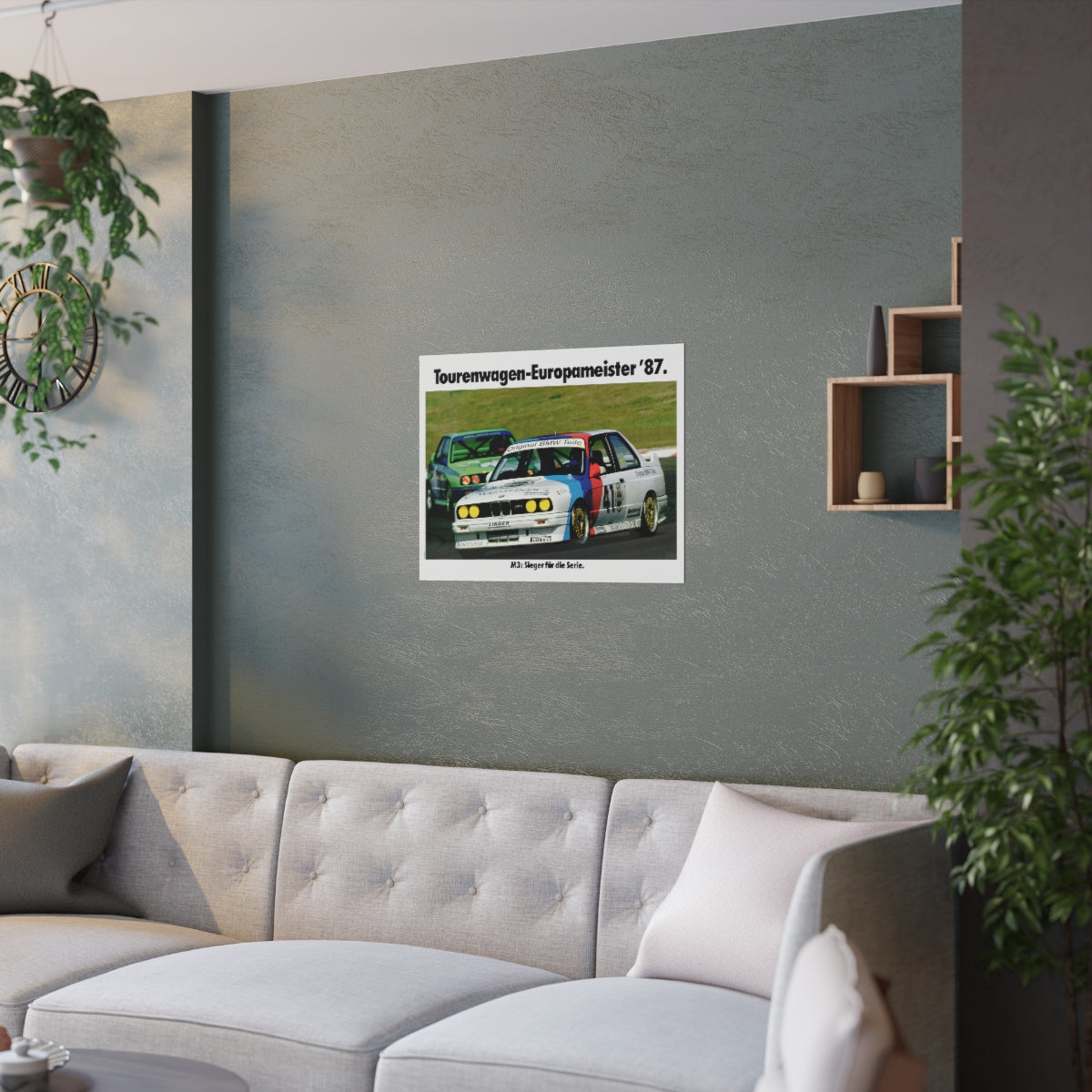 BMW E30 M3 shown in motion, racing on a track. Title above the photo reads European Touring Car Champion 1987. The poster is displayed in a green living room and is hanging over white couch.