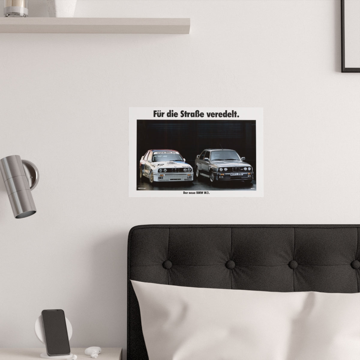 BMW M3 E30 and M3 E30 race car next to each other with text on top that reads "Refined for the street". The poster is displayed in a white bedroom and placed over dark gray headboard.