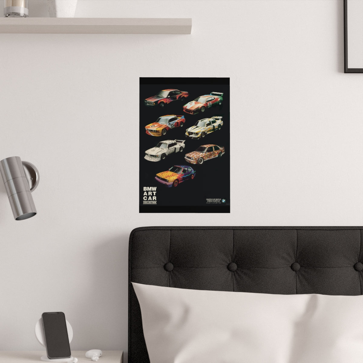 Poster of BMW Art Cars featuring an e24, M1 Procar, two E9 bat mobiles, an e21 race car and two e30 m3 race cars. All are on a black background. The poster is displayed in a white bedroom and placed over dark gray headboard.