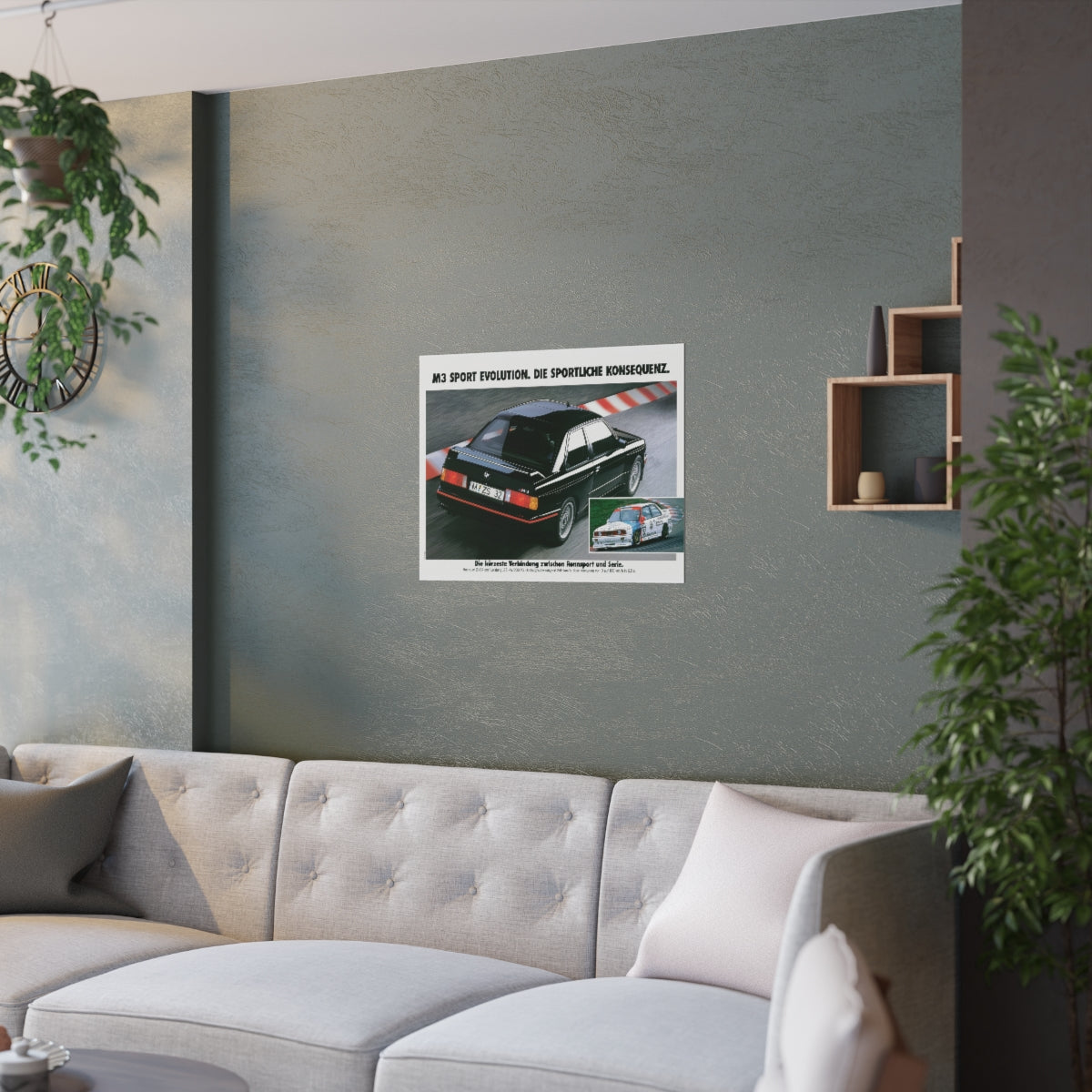 Black BMW E30 M3 Sport Evolution shown in motion, on a racing track. In the lower right corner is a similar picture of an E30 M3 race car. Title above the photo reads M3 Sport Evolution - The Sporting consequence. The poster is displayed in a green living room and is hanging over white couch.