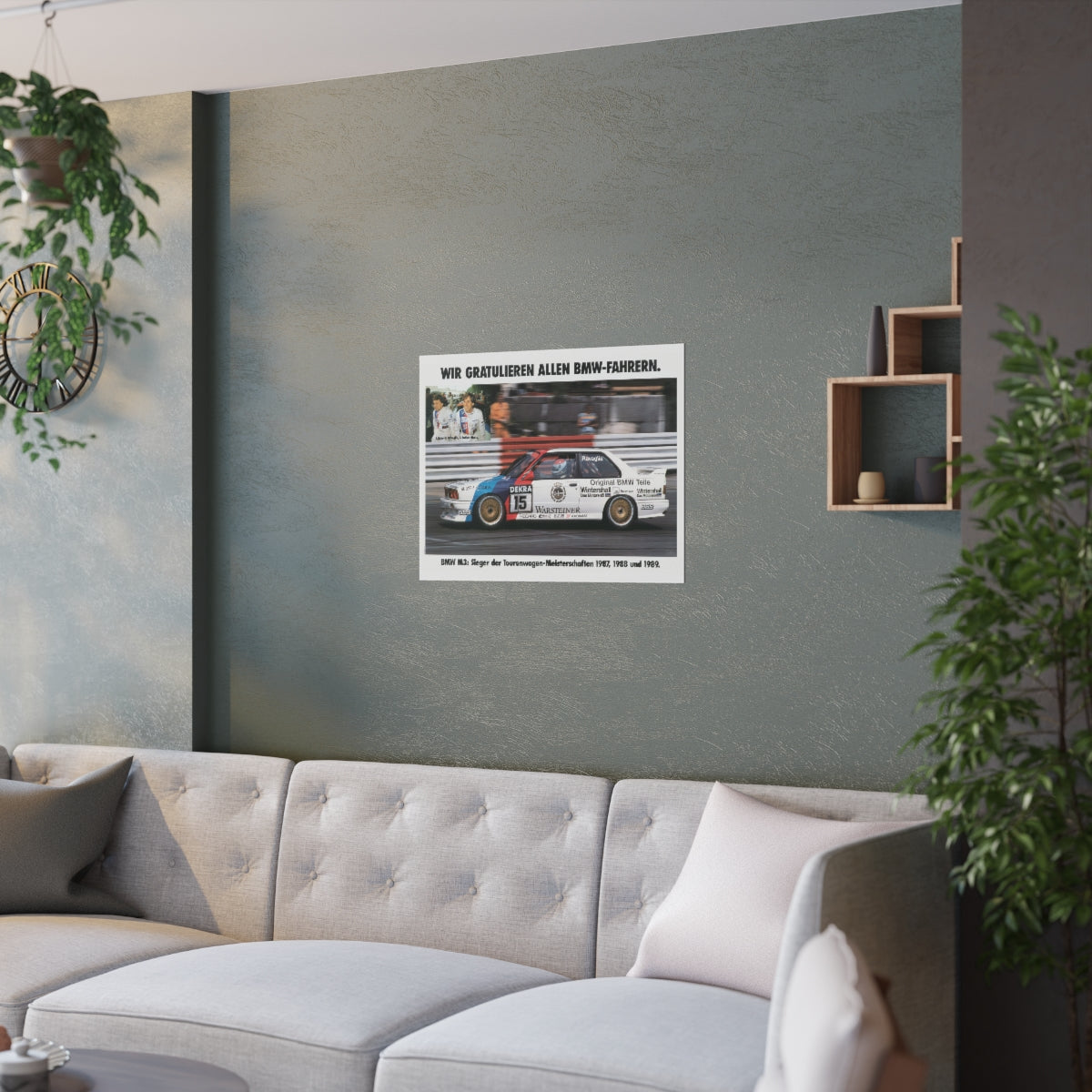 BMW E30 M3 shown in motion, racing on a track. Title above the photo reads Congratulations to all BMW drivers. The poster is displayed in a green living room and is hanging over white couch.