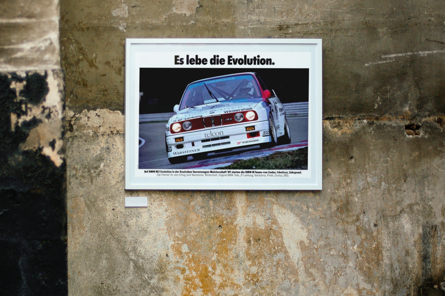 BMW E30 M3 shown in motion, racing on a track. Title above the photo reads Long live Evolution. The frame is displayed on a beautiful concrete wall.