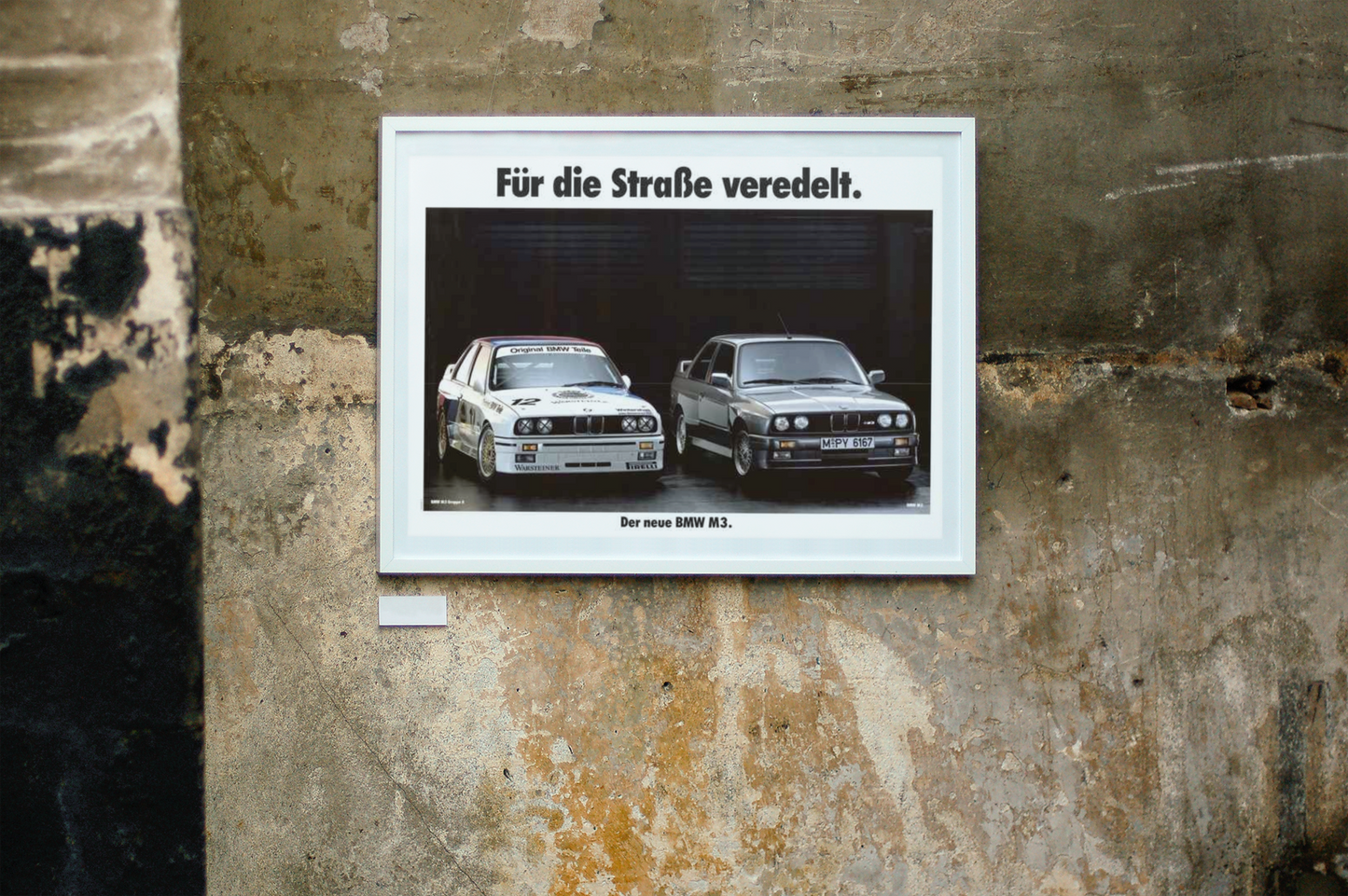 BMW M3 E30 and M3 E30 race car next to each other with text on top that reads "Refined for the street". The frame is displayed on a beautiful concrete wall.