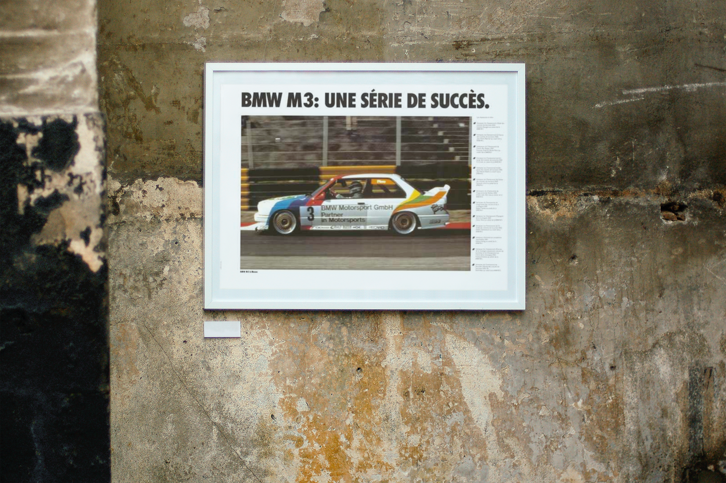 BMW E30 M3 shown in motion, racing on a track. Title above the photo reads BMW M3 a series of successes. The frame is displayed on a beautiful concrete wall.