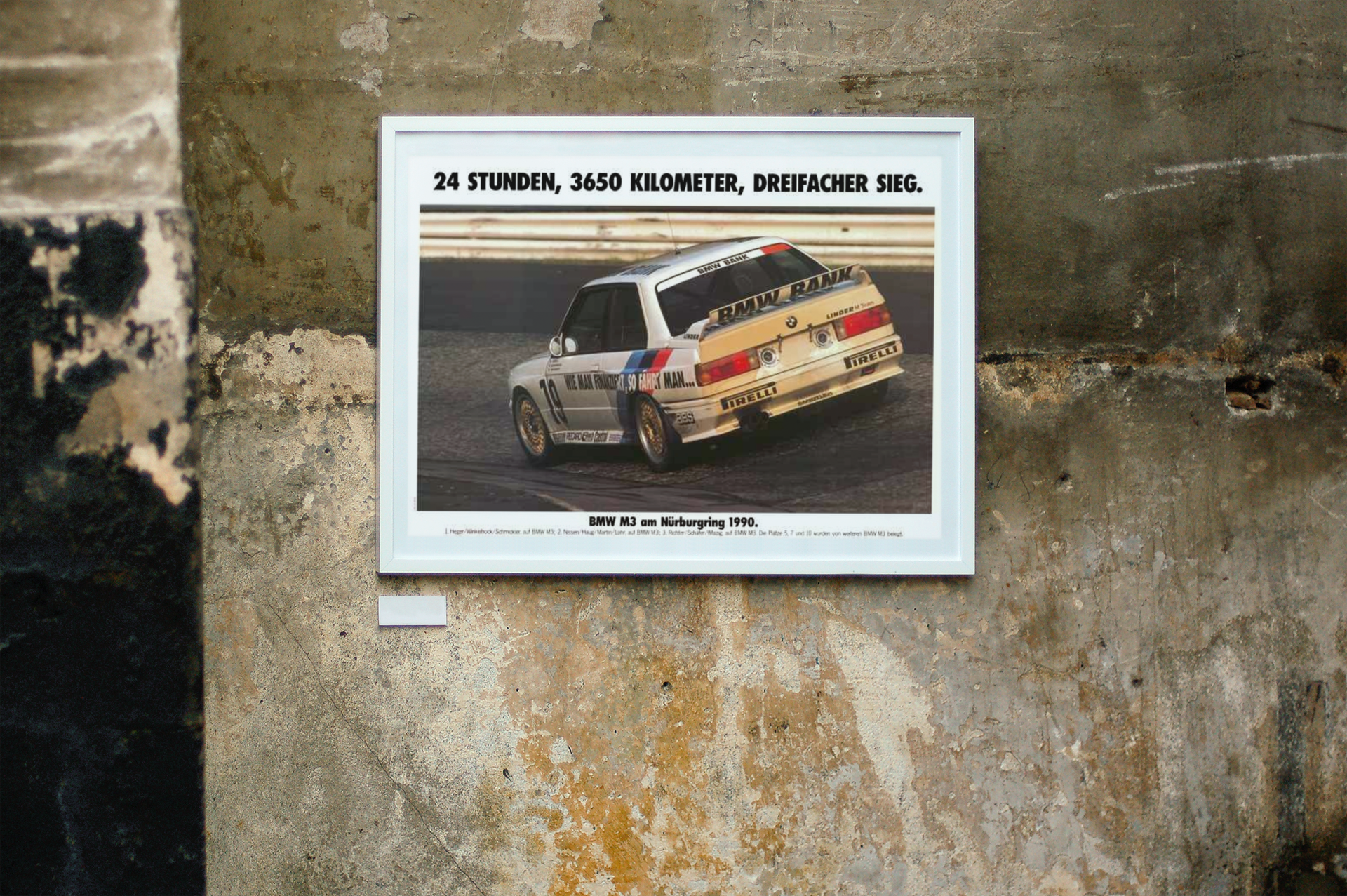 BMW E30 M3 shown racing on the iconic Carousel corner at the Nurburgring track in Germany. Title of the picture reads "24 Hours, 3650 kilometers, triple victory". The frame is displayed on a beautiful concrete wall.